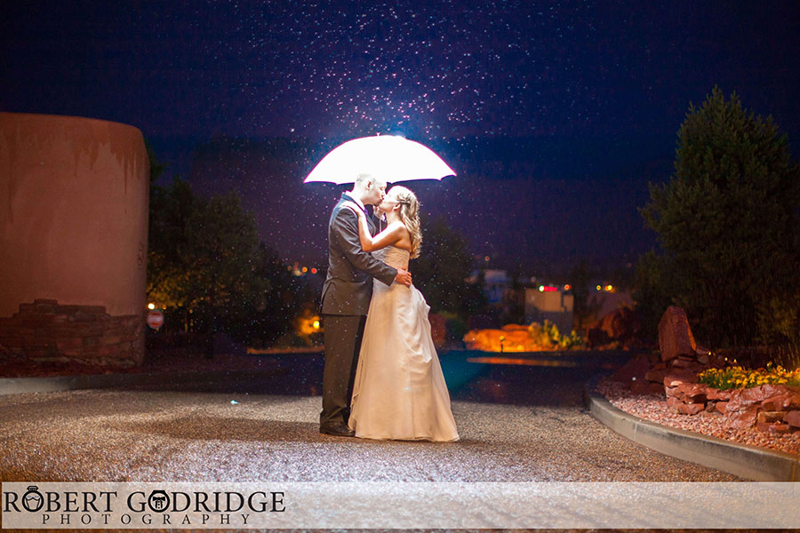 Romantic moment of a couple kissing under a glowing umbrella at Sedona Golf Resort, with sparkling raindrops around them.